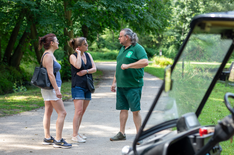 Photo d'un employé du Domaine discutant autour du lac avec 2 dames, à côté de sa voiturette de golf